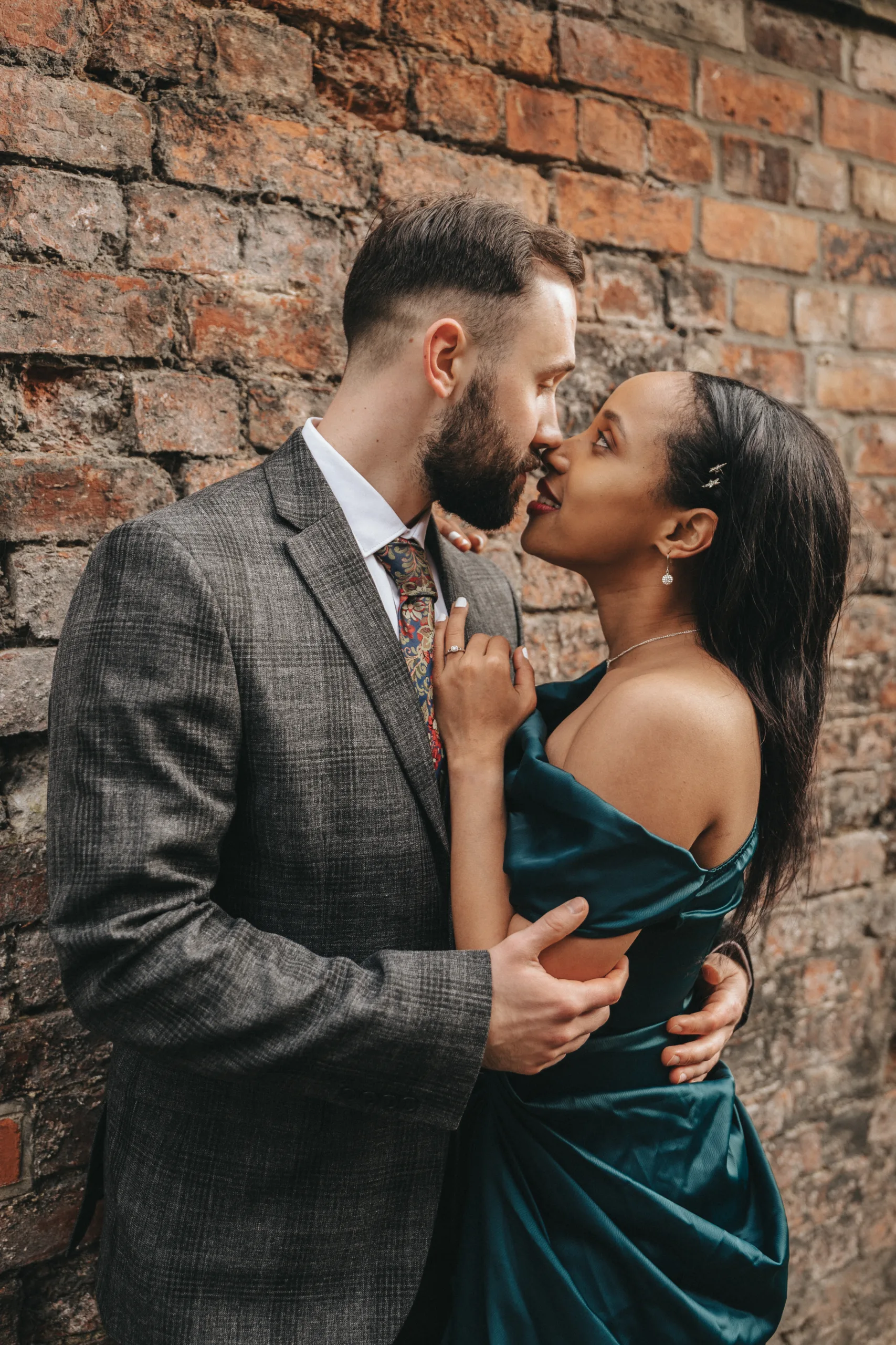 An engaged couple kissing in front of a brick wall captured in Yorkshire.