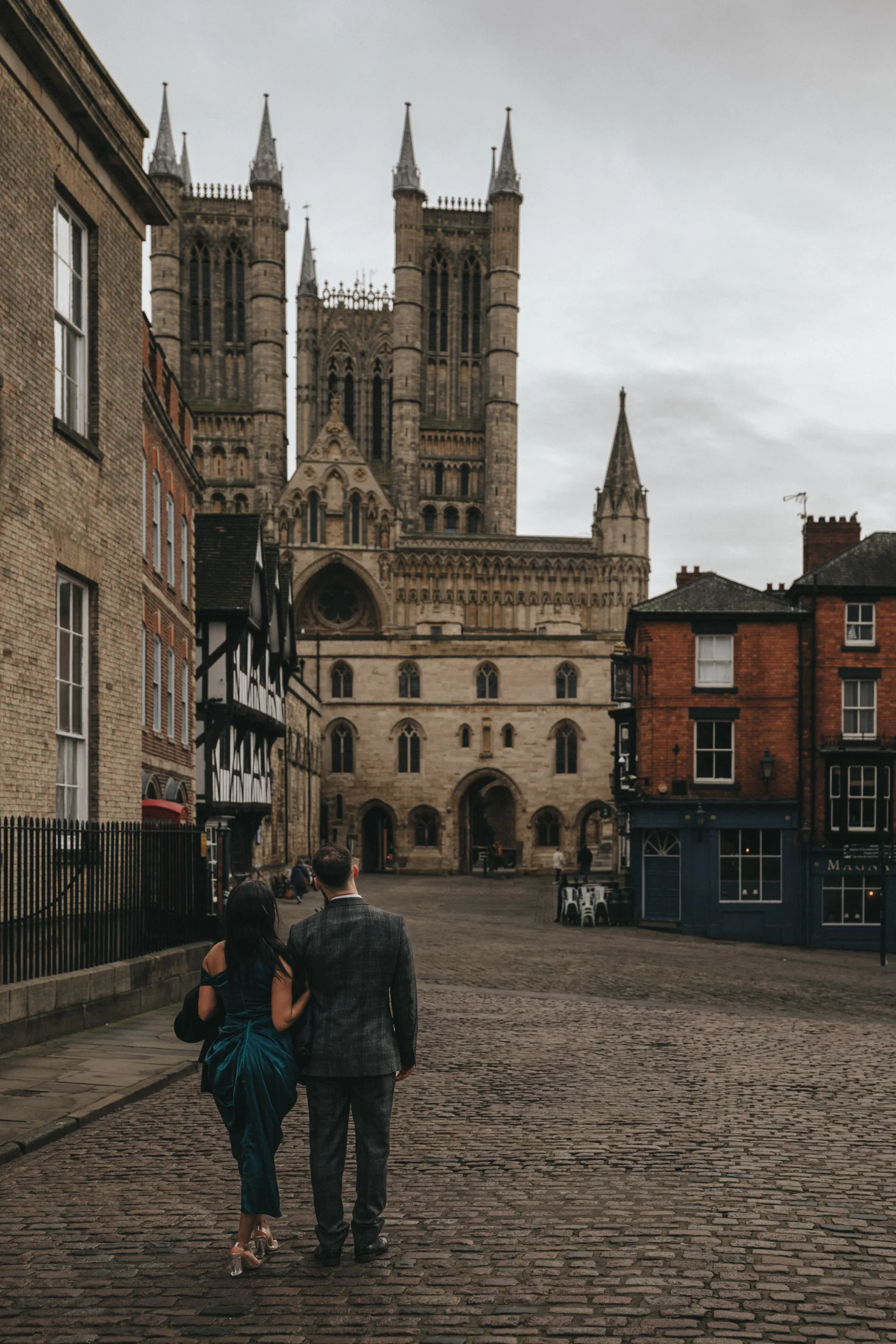 A couple strolling down a cobbled street with a cathedral in the background.