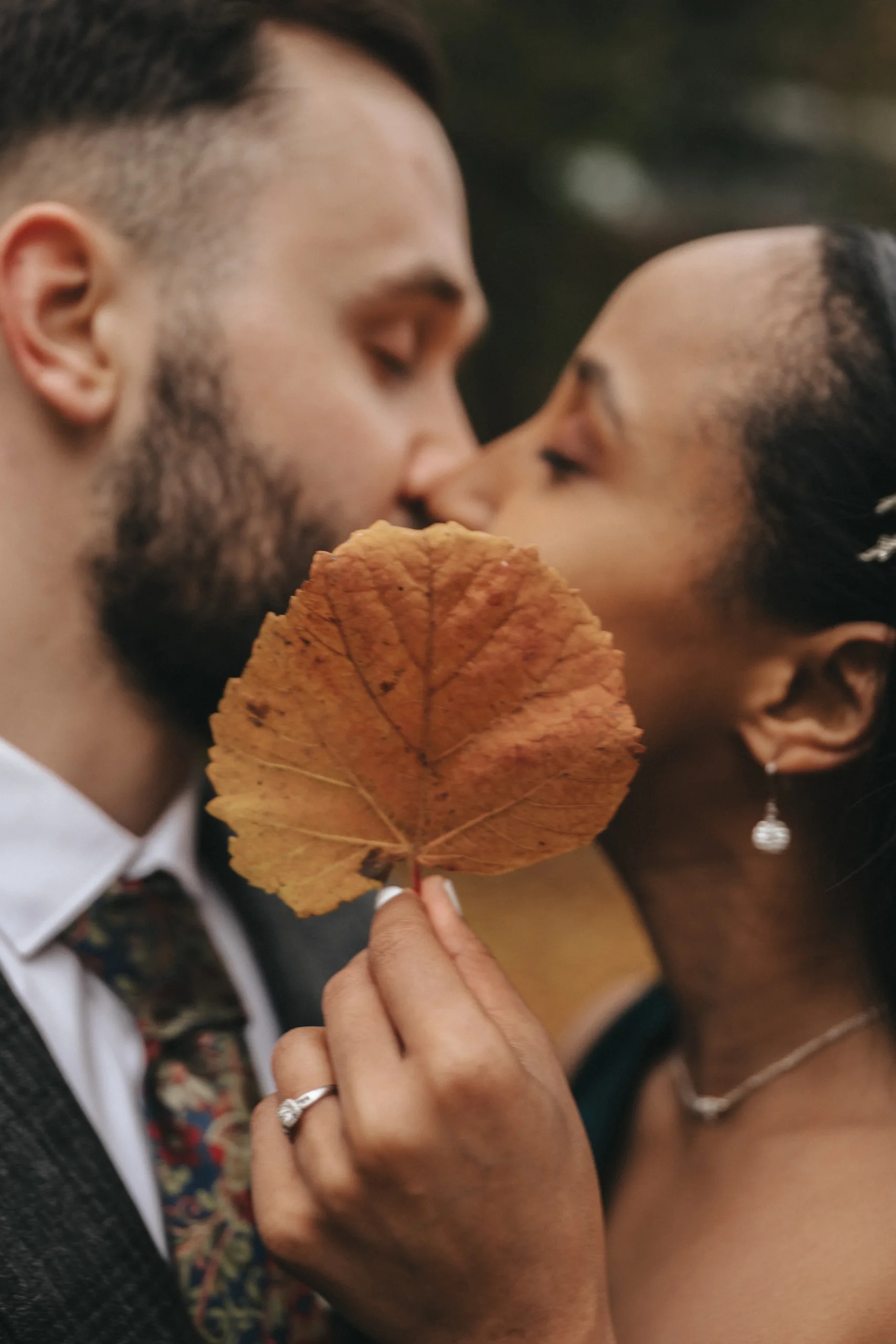 A wedding couple kissing while holding a leaf, captured in Lincolnshire photography.
