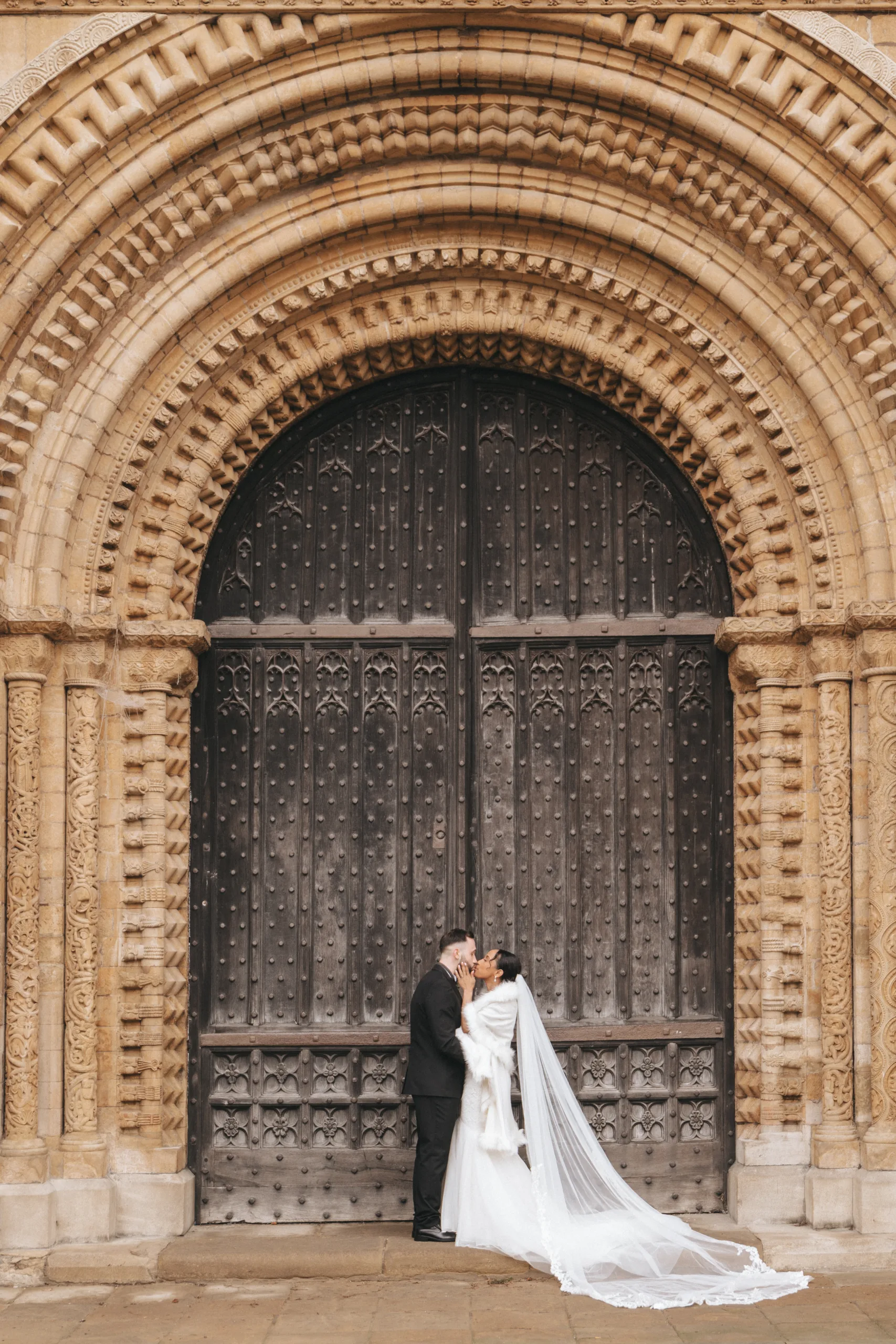 A wedding couple kissing in front of an ornate door, captured by a photographer.