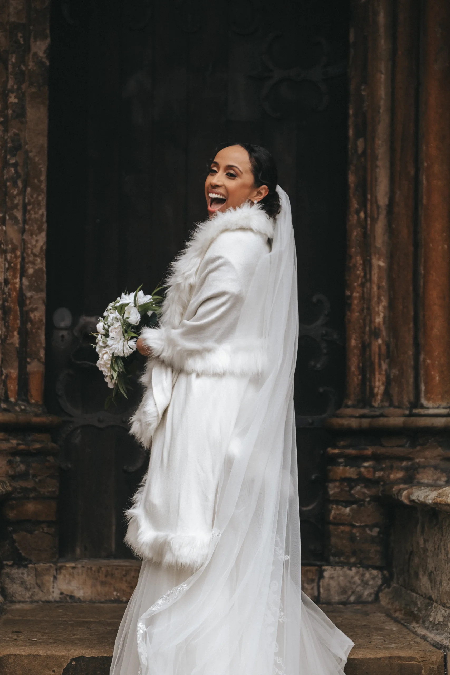 A bride in a white wedding dress laughing in front of a door, captured by a photographer in Lincolnshire.