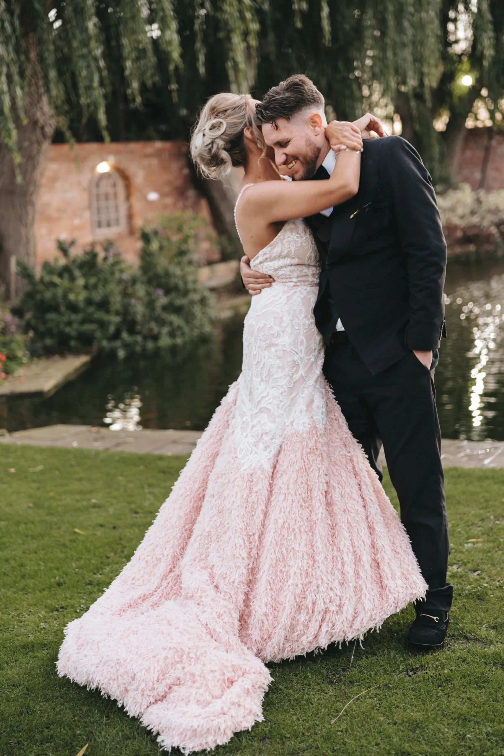 A bride and groom embrace in front of a pond during their photography session.