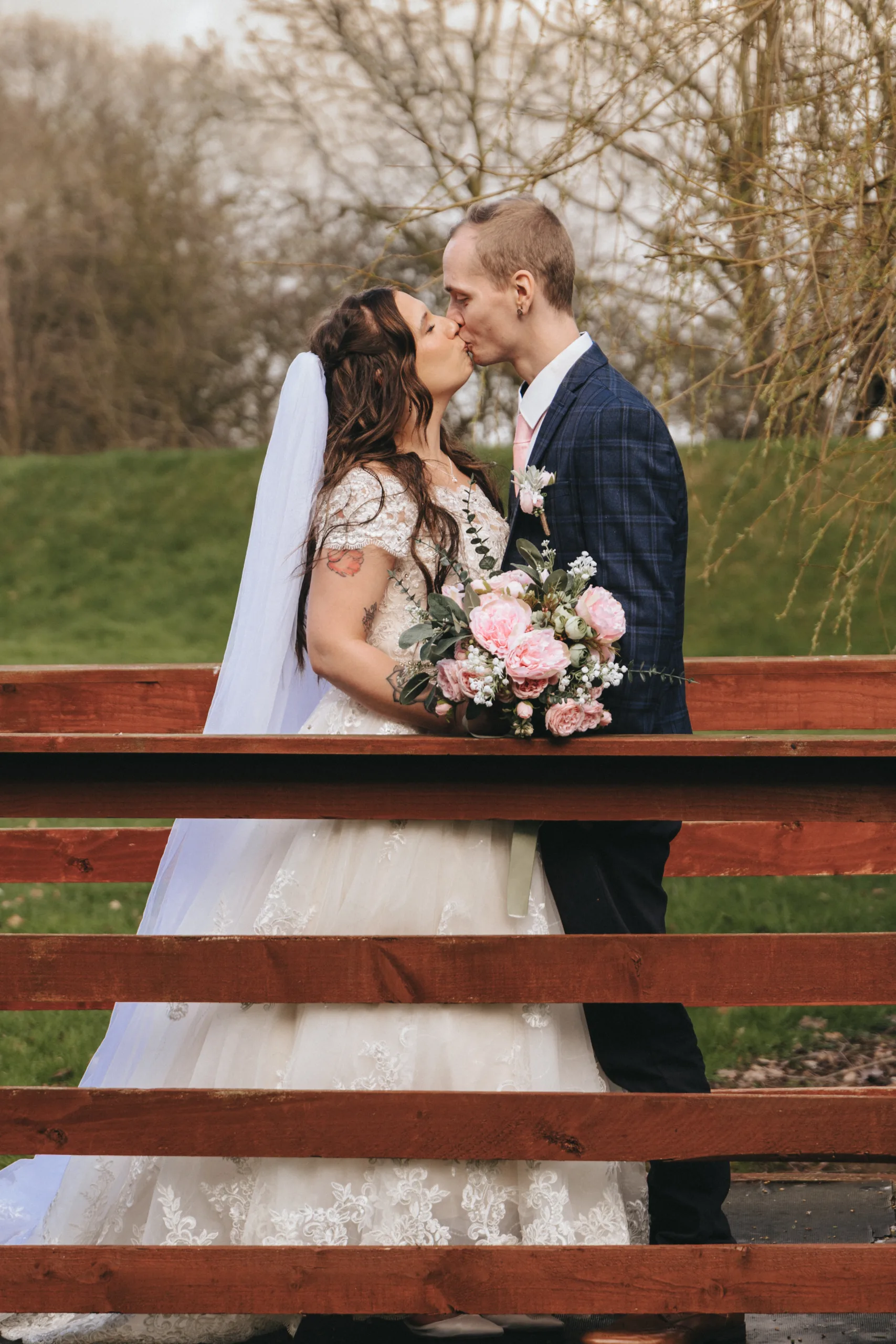 A bride and groom kissing on a wooden bridge.