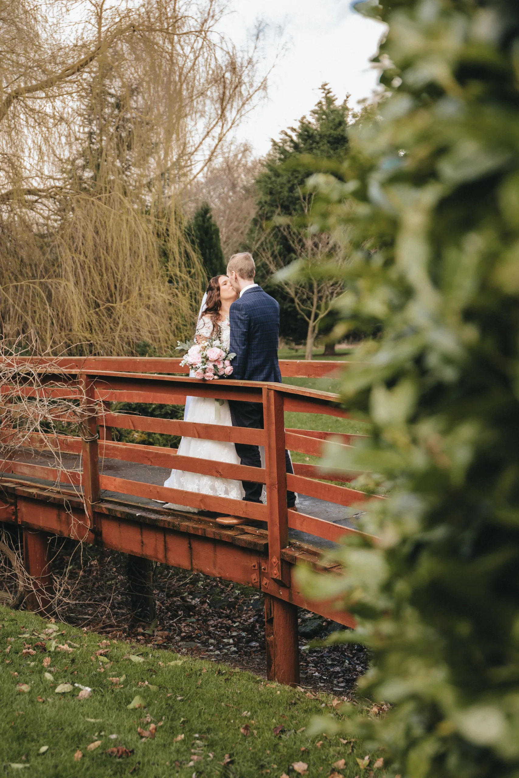 A bride and groom standing on a bridge in a garden.