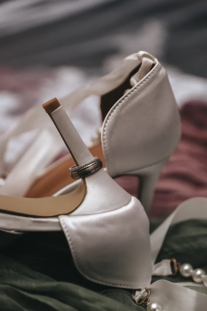 A pair of white high heeled shoes with a ring on the bottom.