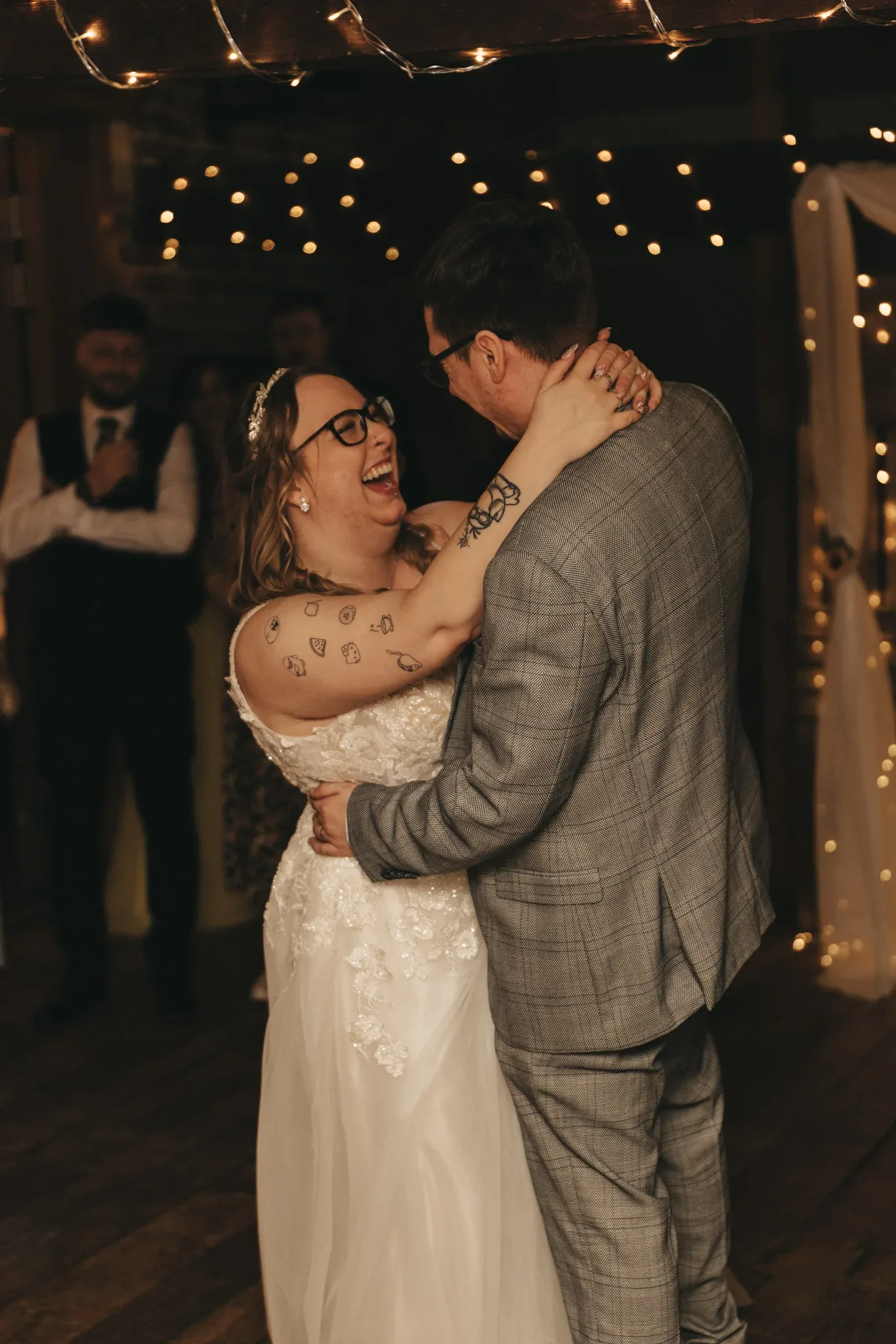 A joyful bride and groom share a heartfelt dance under a canopy of twinkling lights, surrounded by the warm ambiance of their wedding celebration.