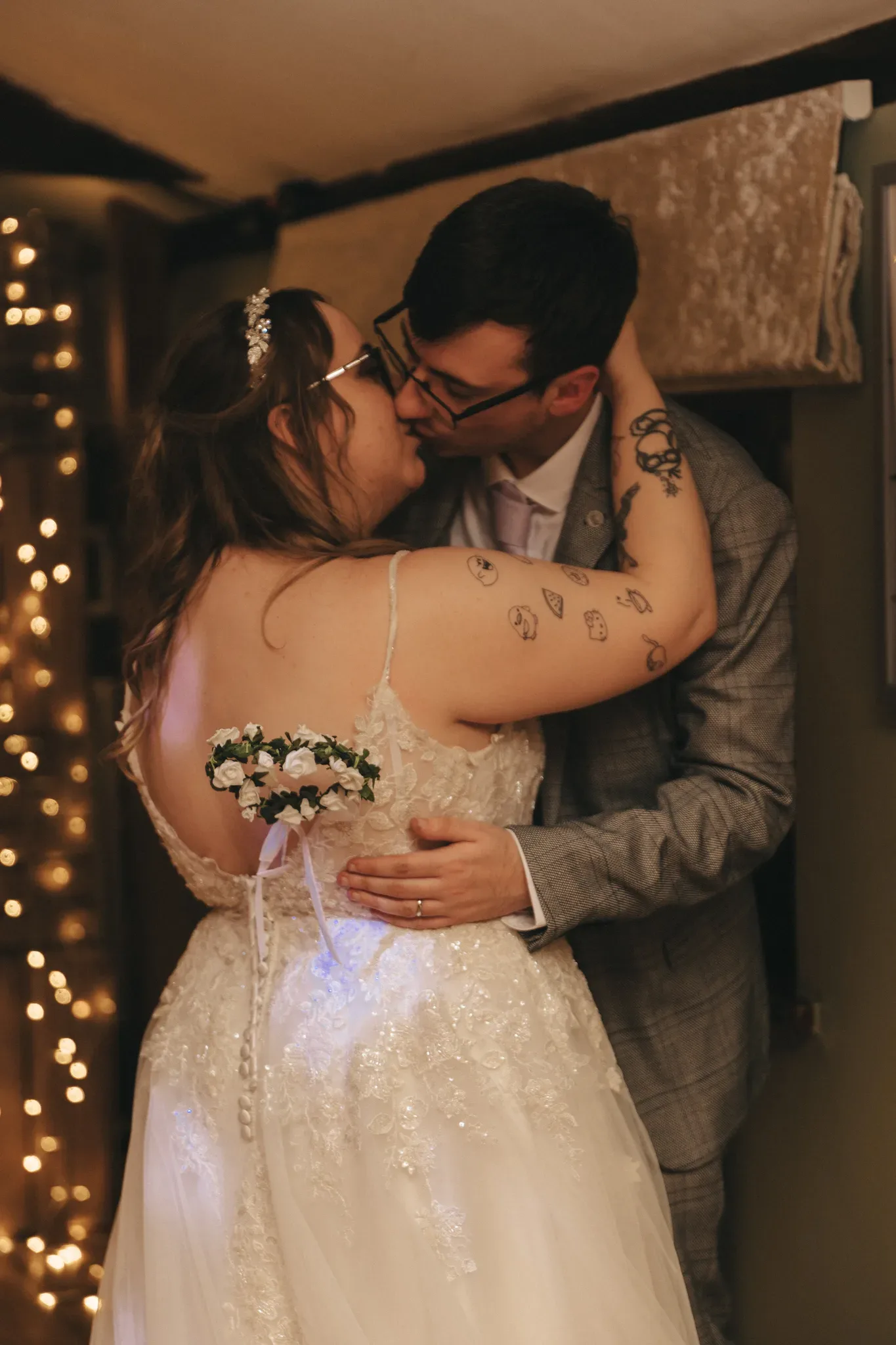A couple in wedding attire shares an intimate embrace and kiss, surrounded by warm ambient lighting and delicate bokeh, symbolizing love and union.