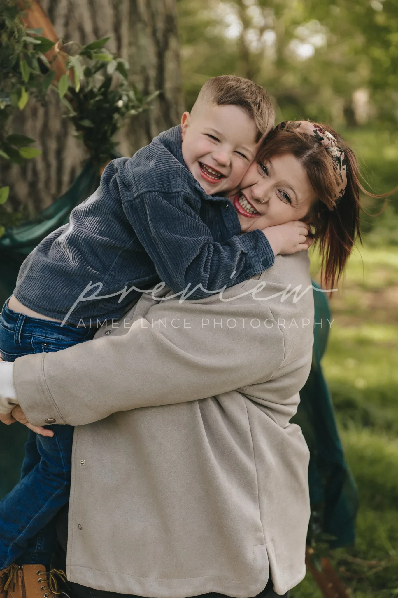 A joyful young boy with short hair hugs a smiling woman named Gabrielle closely in a lush, green park. Both are casually dressed, the boy in a denim jacket and Gabrielle in a beige coat