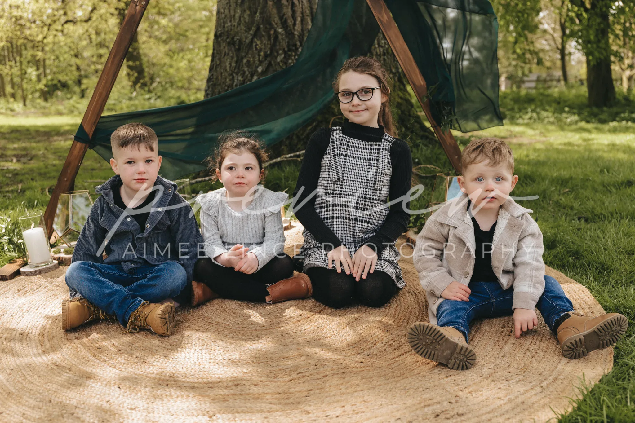 Four children sit under a makeshift tent in a park. From left: a boy in a denim jacket, Gabrielle in a white top, another girl in a plaid dress with glasses, and a