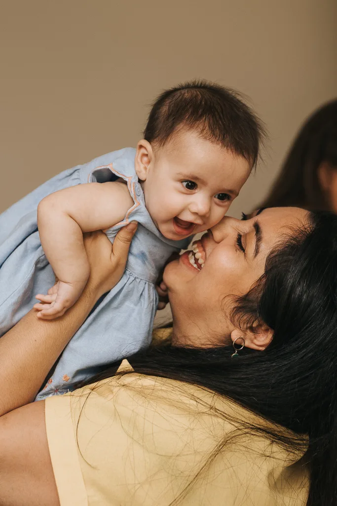 A joyful moment unfolds between the woman, in a yellow top, and her delightful baby. With long dark hair flowing, she lifts the baby high. Dressed in light blue, the baby smiles widely. A blurred background ensures all attention is on their pure expressions of happiness. © Aimee Lince Photography - Wedding photographer in Lincolnshire, Yorkshire & Nottinghamshire