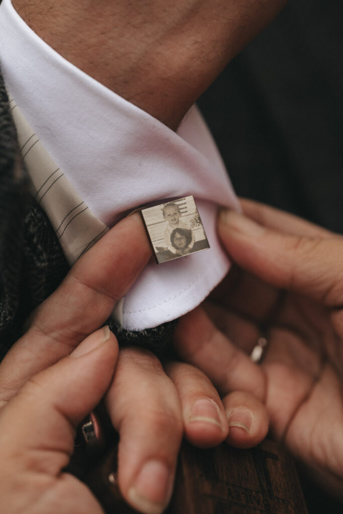 A close-up of a person in a suit with a white shirt, adjusting an elegant cufflink showing a black-and-white image. The gray patterned suit and striped tie hint at an event worthy of Oaklands Hall Hotel's signature style—a setting perfect for capturing timeless wedding photography moments. © Aimee Lince Photography