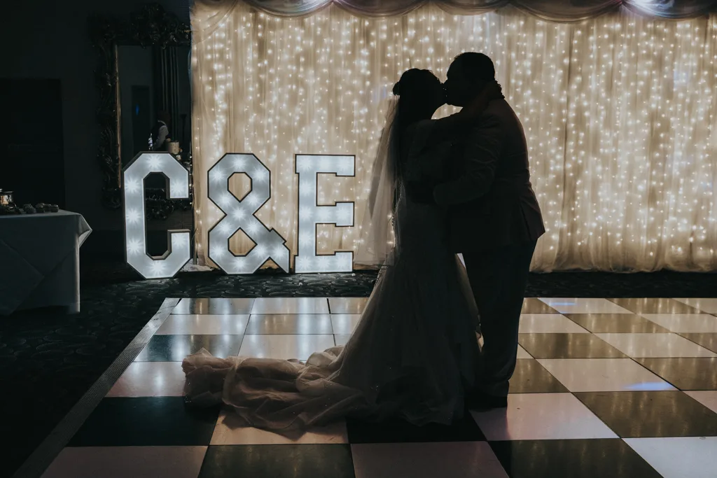 Brackenborough Lakes Resort Hotel Wedding Photos Louth Lincolnshire Chloe & Ethan 612 of 704 © Aimee Lince Photography - 03.05.2025 A bride and groom share a romantic dance on a black and white checkered floor at their Brackenborough wedding, silhouetted against glowing fairy lights. Large illuminated letters “C&E” add to the dreamy atmosphere captured in this stunning photography. © Aimee Lince Photography - Wedding photographer in Lincolnshire, Yorkshire & Nottinghamshire