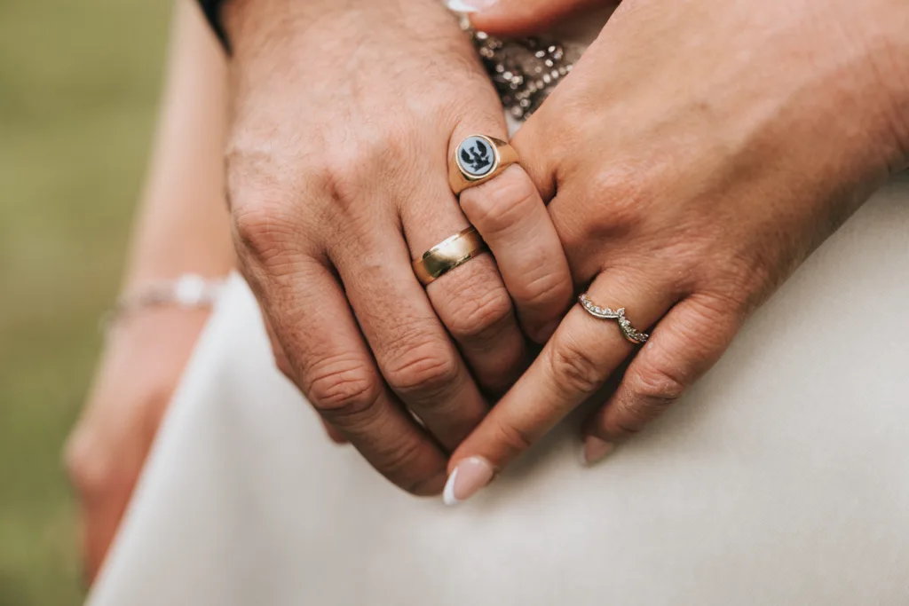 Two hands, likely captured by a Kettering photographer at Rushton Hall, rest gently on white fabric—one with a gold band and silver signet ring, the other with a thin, decorative ring. © Aimee Lince Photography - Wedding photographer in Lincolnshire, Yorkshire & Nottinghamshire
