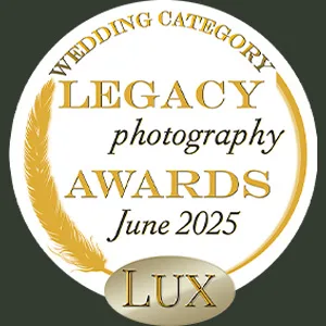 A round badge with a gold feather and text: "Wedding Category LEGACY photography AWARDS June 2025." At the bottom is a gold oval with the word "LUX" inside. The badge has a dark background and a white center. © Aimee Lince Photography - Wedding photographer in Lincolnshire, Yorkshire & Nottinghamshire