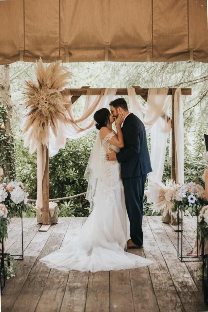 A bride and groom kiss under a wooden arch at Hackness Grange, near Scarborough. Surrounded by lush greenery and floral arrangements, this moment is perfectly captured by their wedding photographer. © Aimee Lince Photography - Wedding photographer in Lincolnshire, Yorkshire & Nottinghamshire