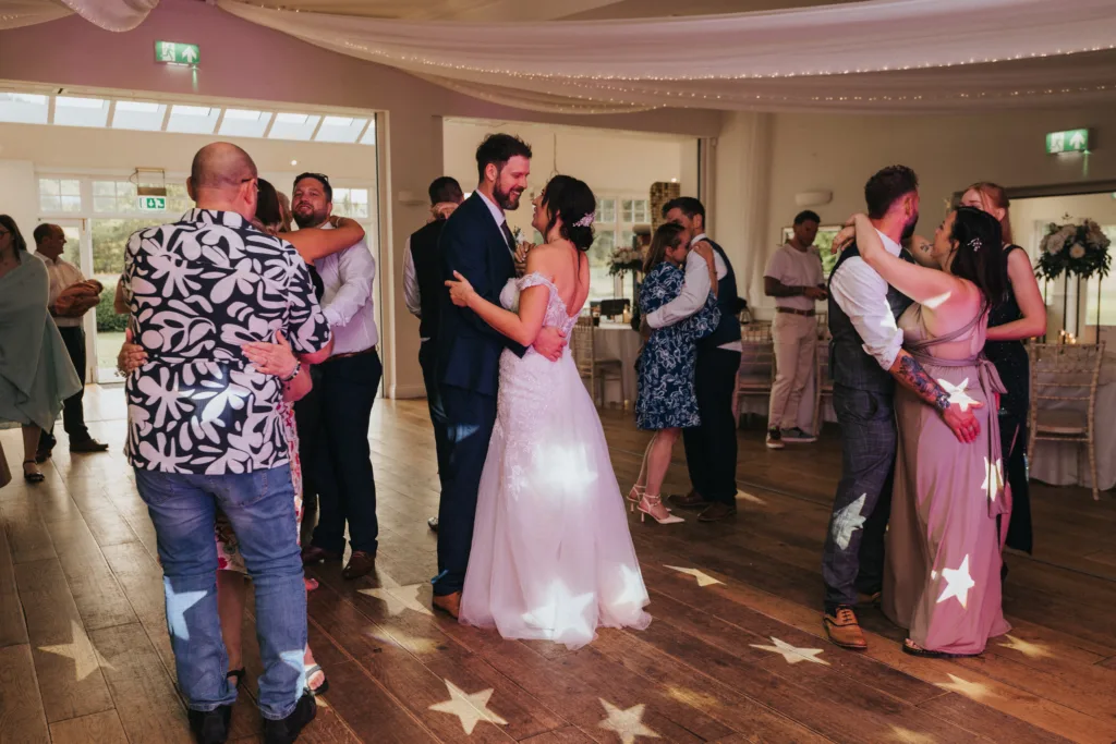 A bride and groom dance together in the center of a warmly lit room at Hackness Grange, surrounded by other couples. Soft sunlight and star-shaped lights illuminate the floor, creating a festive scene for this Scarborough wedding photographer to capture. © Aimee Lince Photography - Wedding photographer in Lincolnshire, Yorkshire & Nottinghamshire