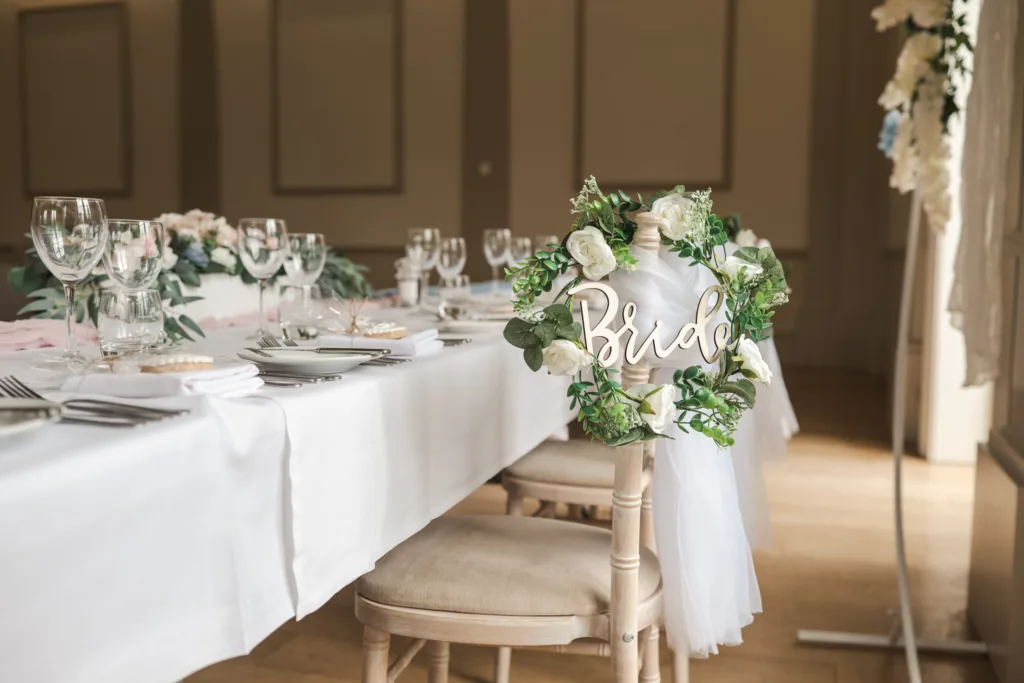 A decorated wedding reception table with white linen, floral arrangements, glassware, and a wooden chair adorned with a "Bride" sign and white flowers. © Aimee Lince Photography, wedding and lifestyle photographer in Lincolnshire