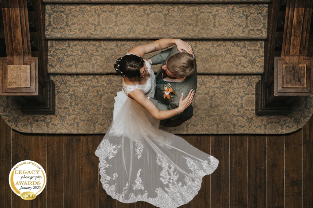 An overhead view of a bride and groom embracing closely on a dark wooden floor at Bourton Hall in Warwickshire. Captured in a romantic and intimate moment on their wedding day. The bride wears a white dress and the groom is in a suit. © Aimee Lince Photography, Wedding photographer in Lincolnshire