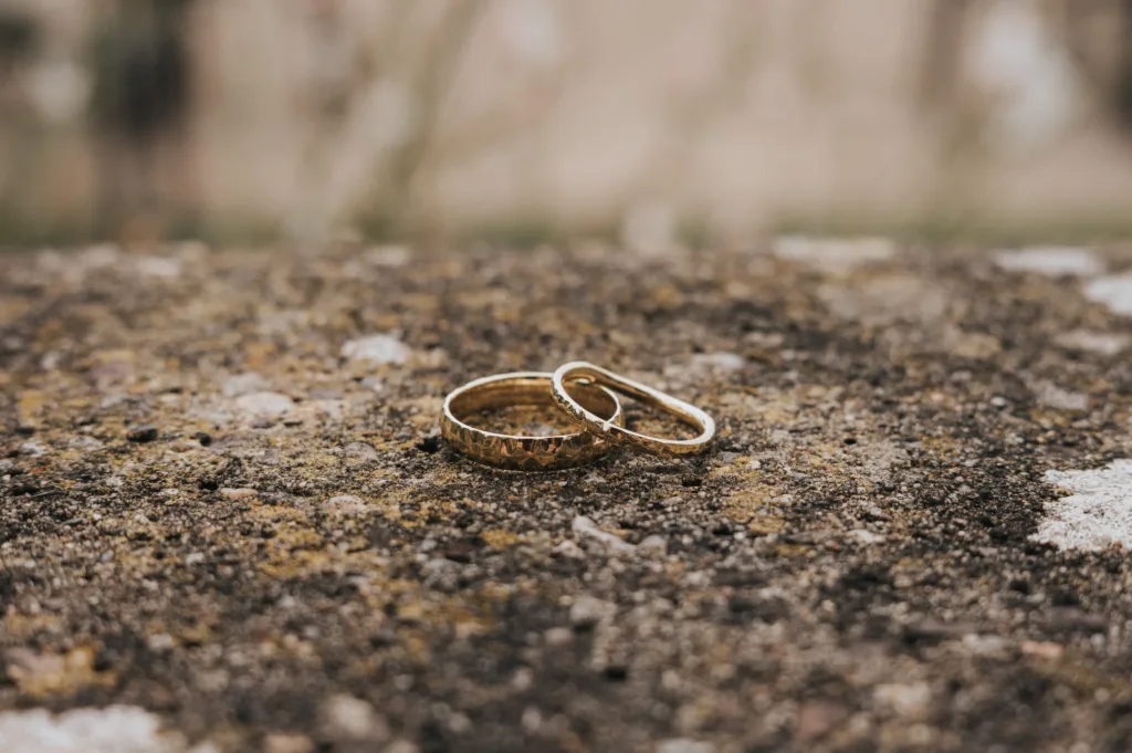 Two gold rings rest on a rough, textured stone surface, with a soft, blurred background of natural colours. © Aimee Lince Photography, Wedding photographer in Lincolnshire