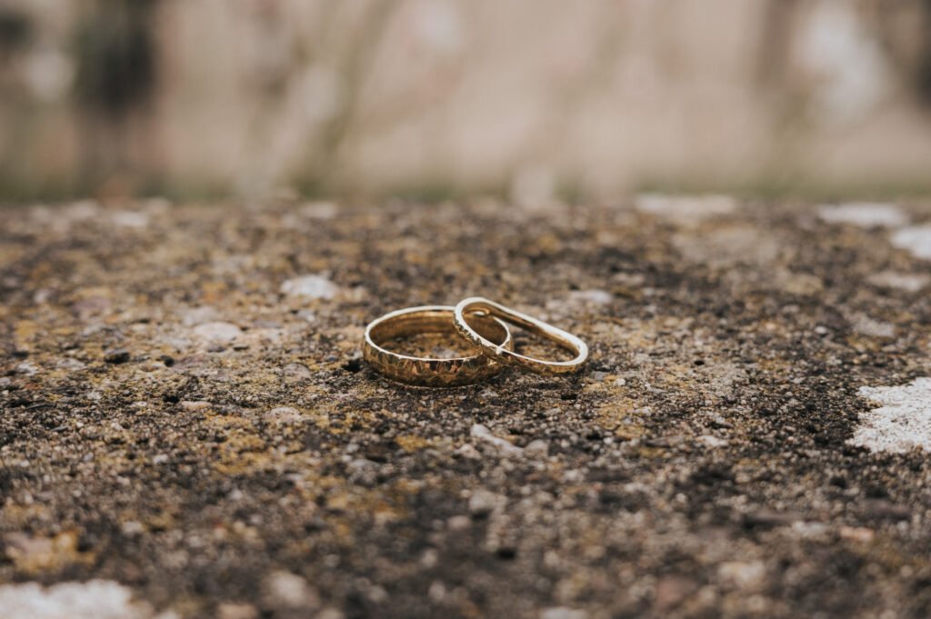 Two gold rings rest on a rough, textured stone surface, with a soft, blurred background of natural colours. © Aimee Lince Photography, Wedding photographer in Lincolnshire